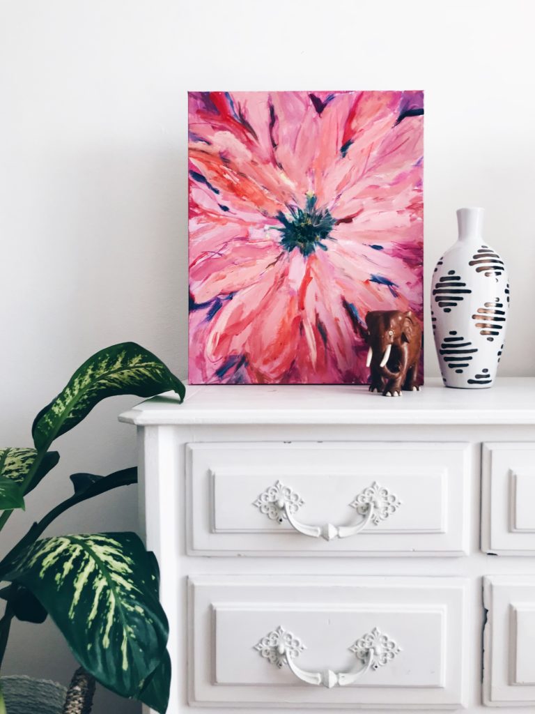 This is an image of a pink flower wall art canvas sitting on top of a white dresser to show an example of how to decorate with pink. 